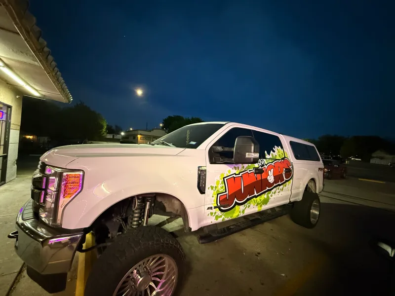 Lifted white Ford F-250 at night with Junior's graffiti-style door decals