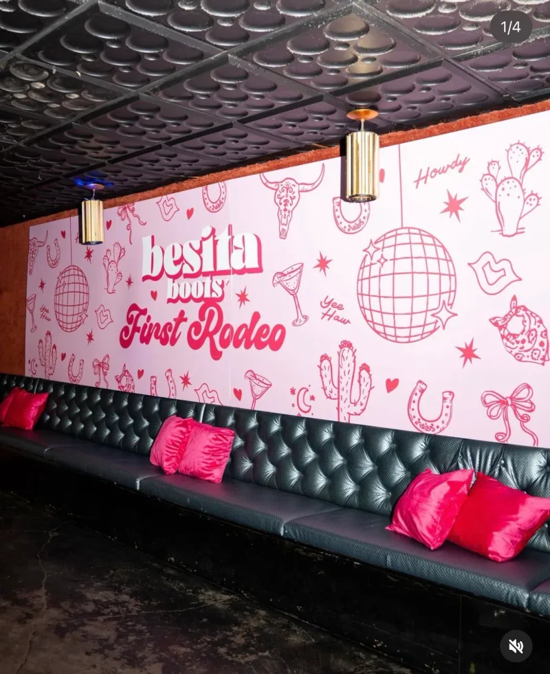 Pink printed wall mural reading Besita Boots First Rodeo behind a black leather banquette