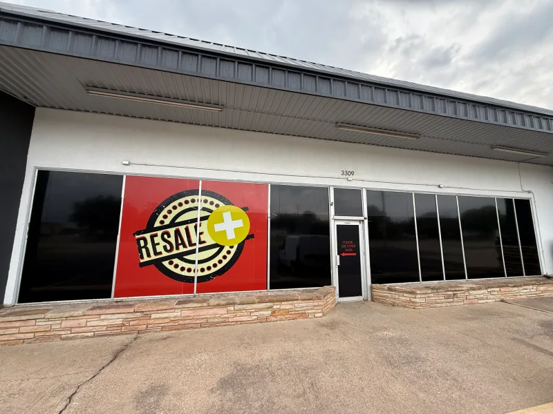 Retail storefront window covered with a large printed Resale+ logo graphic